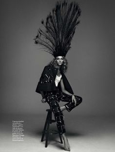 a woman sitting on top of a stool next to a chair with feathers in it