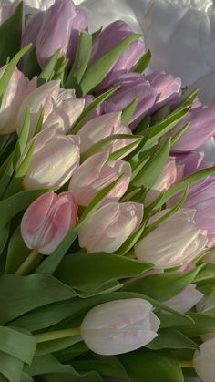 a bouquet of pink and white tulips with green leaves in the middle, on a bed