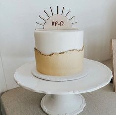 a white cake sitting on top of a table next to a wooden sign that says one