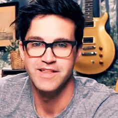 a young man wearing glasses in front of guitars