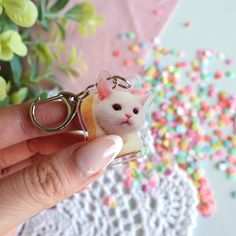 a hand holding a keychain with a small white cat on it's side