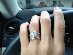 a person's hand on the steering wheel of a car with two engagement rings