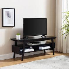 a flat screen tv sitting on top of a wooden stand in front of a window