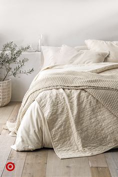 a bed with white linens and pillows in a room next to a potted plant