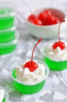 three small cups filled with whipped cream and cherries on top of a tablecloth