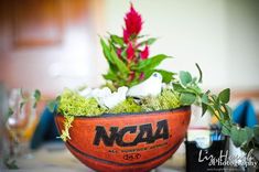 an orange bowl filled with moss and flowers on top of a table next to wine glasses