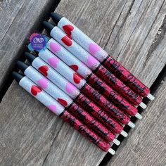 six pens with hearts painted on them are lined up in a row against a wooden surface