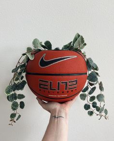 a person holding a basketball in front of a white wall with ivy growing on it