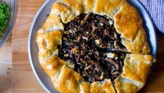 a pie with mushrooms on it sitting on a plate next to a bowl of salad