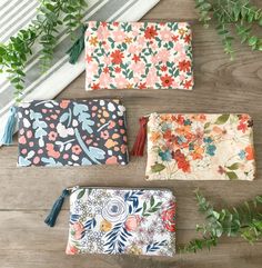 three floral pouches with tassels on top of a wooden table next to green plants