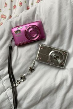 a pink camera sitting on top of a bed next to a lanyard chain necklace