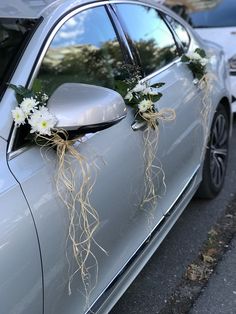 a silver car with white flowers and grass tied to it