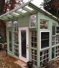 a small green house sitting in the middle of a forest with lots of leaves on the ground