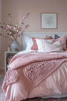 a bed with pink comforter and pillows in a bedroom next to a flower vase