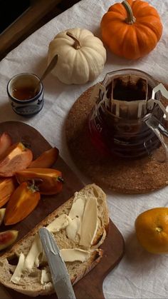 bread, apples, and oranges are on a table next to a tea pot