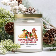 a christmas candle with two dogs on it and pine cones in the background, surrounded by evergreen branches