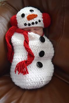 a baby wearing a crocheted snowman hat and scarf on top of a brown couch