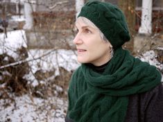 a woman wearing a green hat and scarf in front of snow covered ground with trees