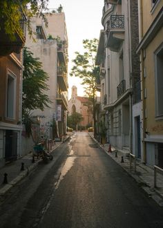 an empty street with people sitting on the curb and buildings in the backround