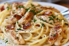 a white plate topped with pasta covered in chicken and bacon sauce, garnished with parsley