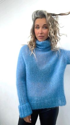 a woman with blonde hair wearing a blue sweater and black leggings stands in front of a white wall