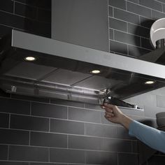 a woman is adjusting the lights on an oven hood in a kitchen with gray tile walls