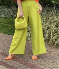 a woman wearing bright yellow pants and an orange top holding a handbag in her right hand