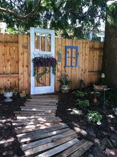 a wooden path leading to a white door in a fenced area with trees and flowers