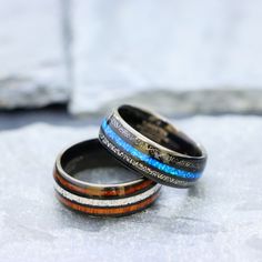 two wedding bands with blue and orange inlays are sitting on top of each other