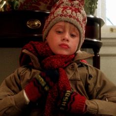 a young boy wearing a hat and scarf sitting in front of a table with presents on it