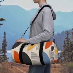 a woman carrying a colorful duffel bag on her back with mountains in the background