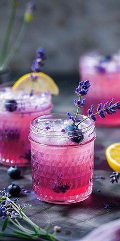 two glasses filled with pink lemonade and lavender sprigs next to sliced lemons