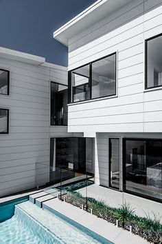 an empty swimming pool in front of a white house with large windows and balconies