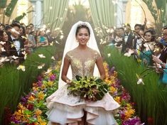 a woman in a wedding dress standing next to a flower garden with people taking pictures behind her