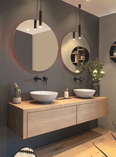 two round mirrors are above the sinks in this modern bathroom with wood cabinets and gray walls