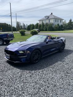 two people in a blue sports car parked on gravel