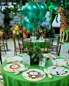 a green table topped with plates covered in animal themed paper napkins next to balloons