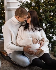 a man and woman sitting on the floor next to a christmas tree holding each other