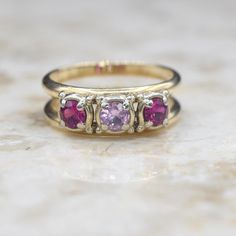 Vintage 14k gold ring with a split band, set with one central pink sapphire with a ruby on either side.  The stones are set in white gold. Era: c.1960s Markings: GB-14k Materials: 14k gold, synthetic pink sapphire, synthetic ruby (3.96mm each) Ring Size: 6.5 Weight: 4.2 grams Condition: Excellent vintage condition with minor surface wear from age  Shipping is free in the United States Follow us on Instagram @LUXXORVintage Pink Three-stone Sapphire Jewelry, Gold Multi-stone Pink Sapphire Ring, Pink Sapphire Ruby Ring With Multi-stone For Gift, Pink Multi-stone Ruby Ring As A Gift, Vintage 14k Gold Multi-stone Ruby Ring, 14k Gold Ring, Three Stone Rings, Multi Stone Ring, Three Stone