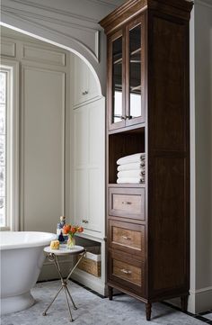 a white bath tub sitting next to a tall wooden cabinet