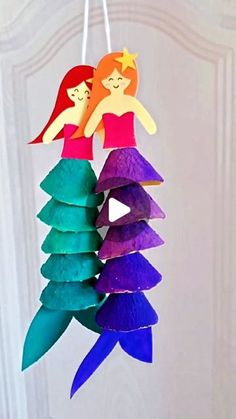 two paper mermaids hanging from strings in front of a white door with an ornament