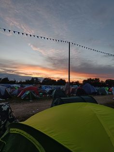 many tents are set up on the ground in front of an orange sky at sunset