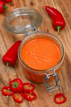 a jar filled with sauce sitting on top of a wooden table next to red peppers