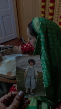 a woman holding up an old photo in front of her face and wearing a green shawl