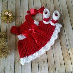 a red and white crocheted baby dress with matching booties sits on a wooden floor