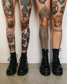 two women with tattoos on their legs standing next to each other, both wearing black combat boots