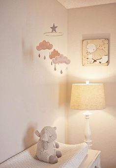 a teddy bear sitting on top of a white crib next to a lamp and painting