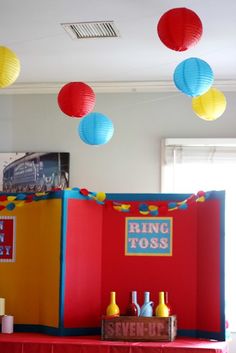 some paper lanterns are hanging from the ceiling above a red table with yellow and blue decorations