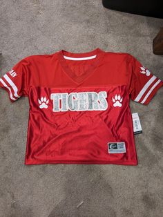 a red football jersey with the word tigers on it and paw prints is laying on the floor