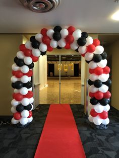 a red, white and black balloon arch with a red carpet on the floor next to it